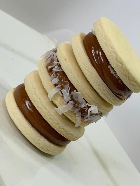 Three sandwich cookies made with pale yellow wafers filled with chocolate spread and shredded coconut flakes