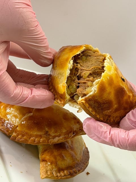Hands in pink gloves breaking open a golden pastry filled with meat curry
