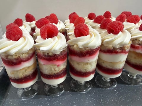 Individual dessert cups with layered cake, cream, and raspberry coulis, topped with fresh raspberries and whipped cream