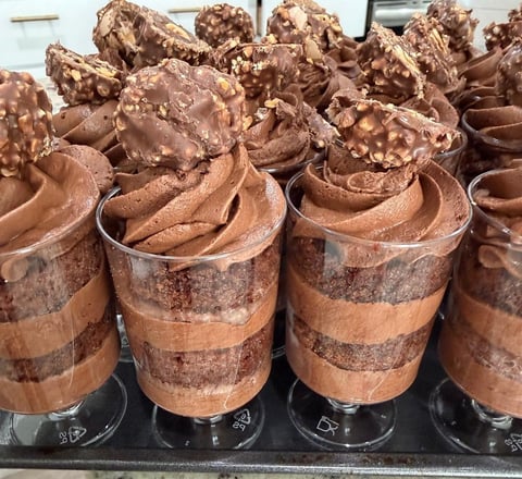 Display of chocolate mousse cups topped with whipped cream and chocolate pieces in clear containers on a black tray