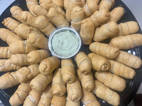 Platter of golden-brown crescent-shaped pastries arranged in a circle around a small bowl of light green dip